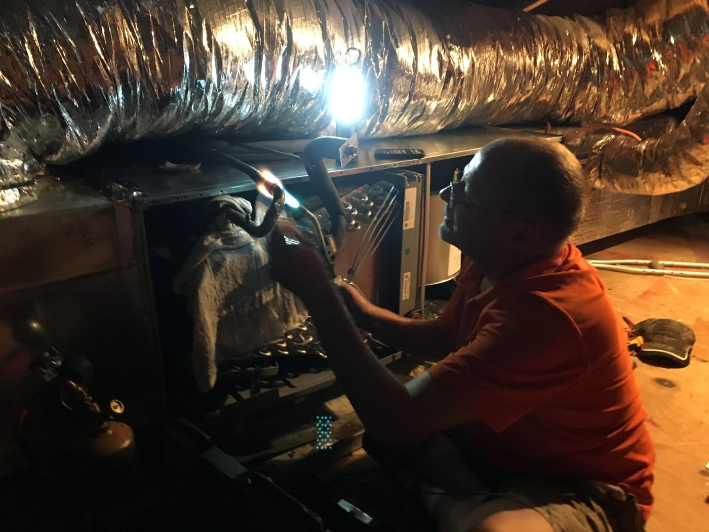 Technician working beneath insulated ductwork in an attic