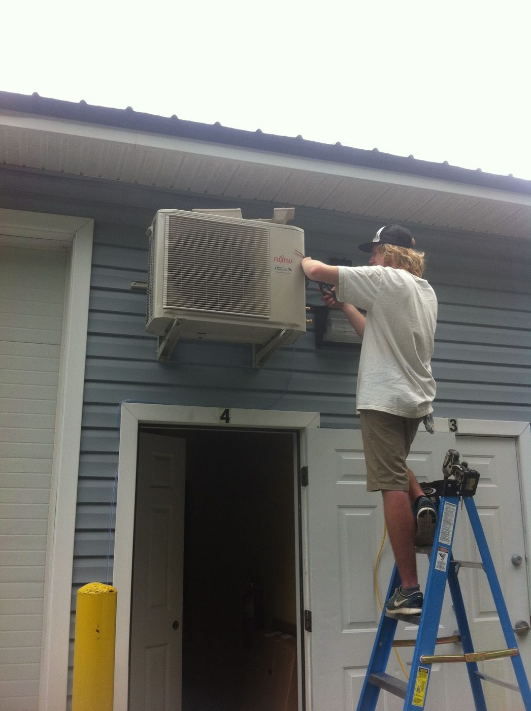 Technician on a ladder servicing a wall-mounted ductless unit