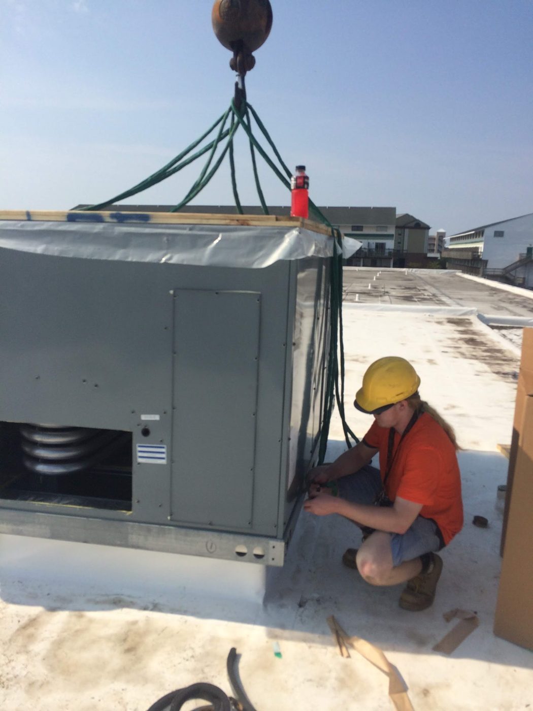 Technician wiring a commercial rooftop unit as it is set by crane