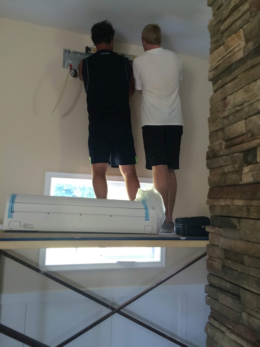 Two technicians mounting a ductless mini-split indoor unit