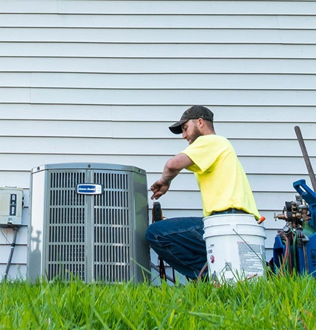 Technician servicing an American Standard air conditioner beside a home