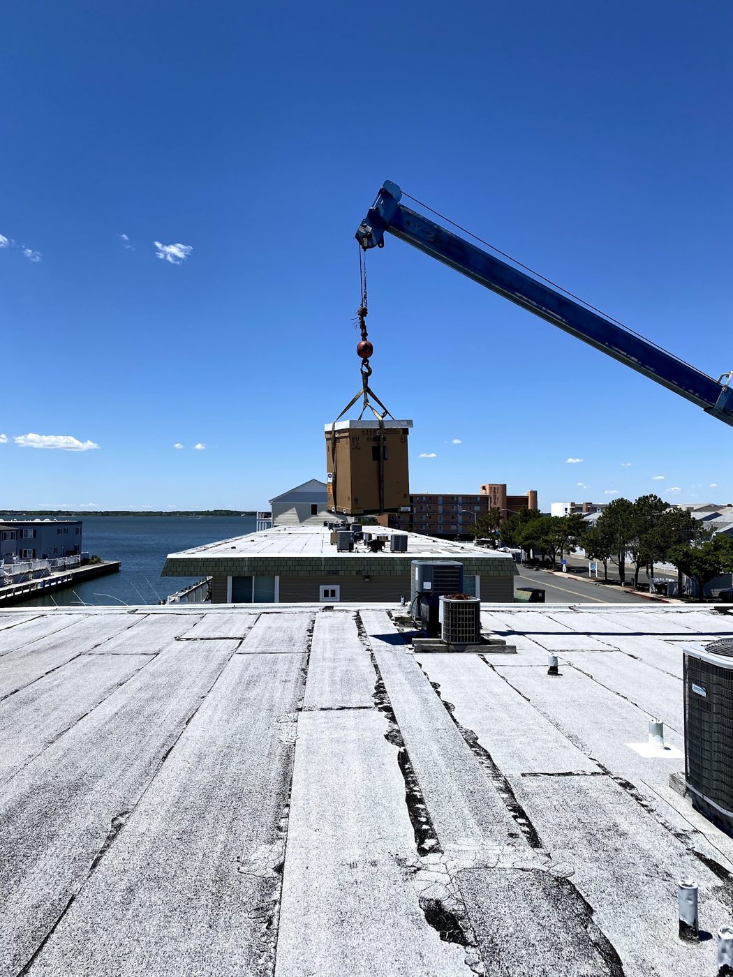 Crane lifting an HVAC unit onto a bayside rooftop