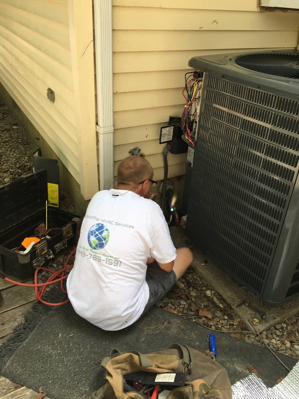Technician servicing an outdoor condenser beside a home