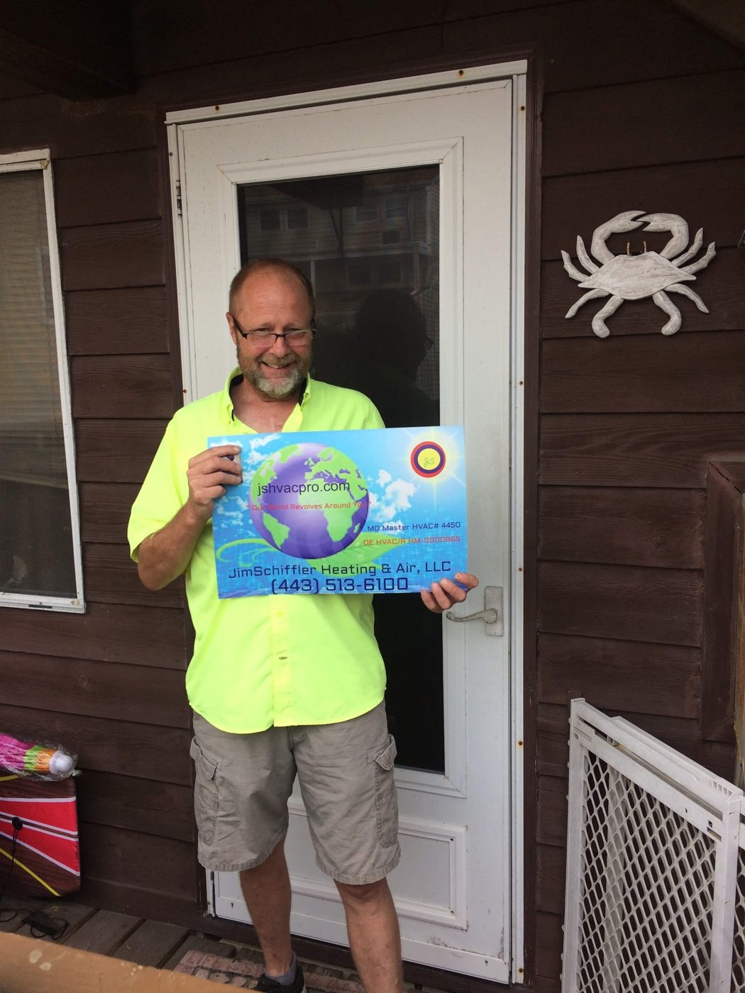 Jim Schiffler holding a company sign outside a coastal home