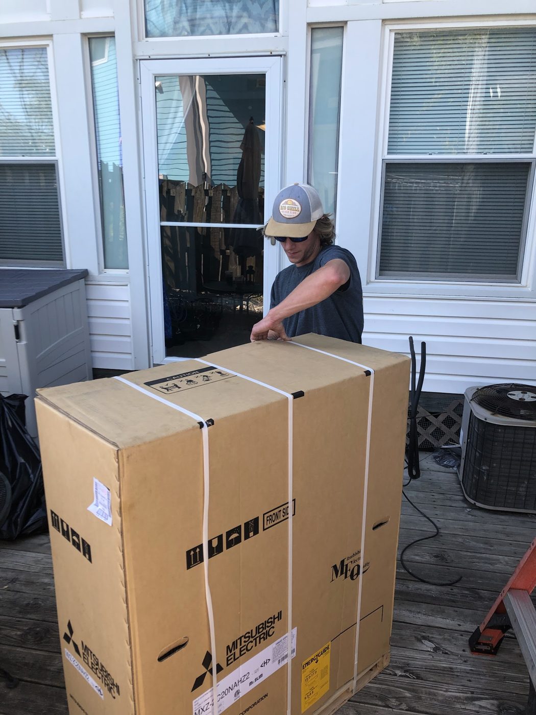 Technician unboxing new Mitsubishi Electric equipment on a deck