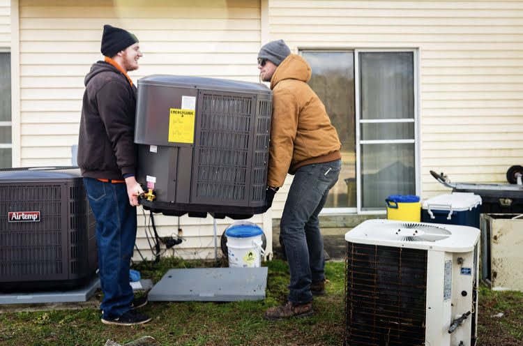 Two Jim Schiffler crew members moving a replacement outdoor unit into place