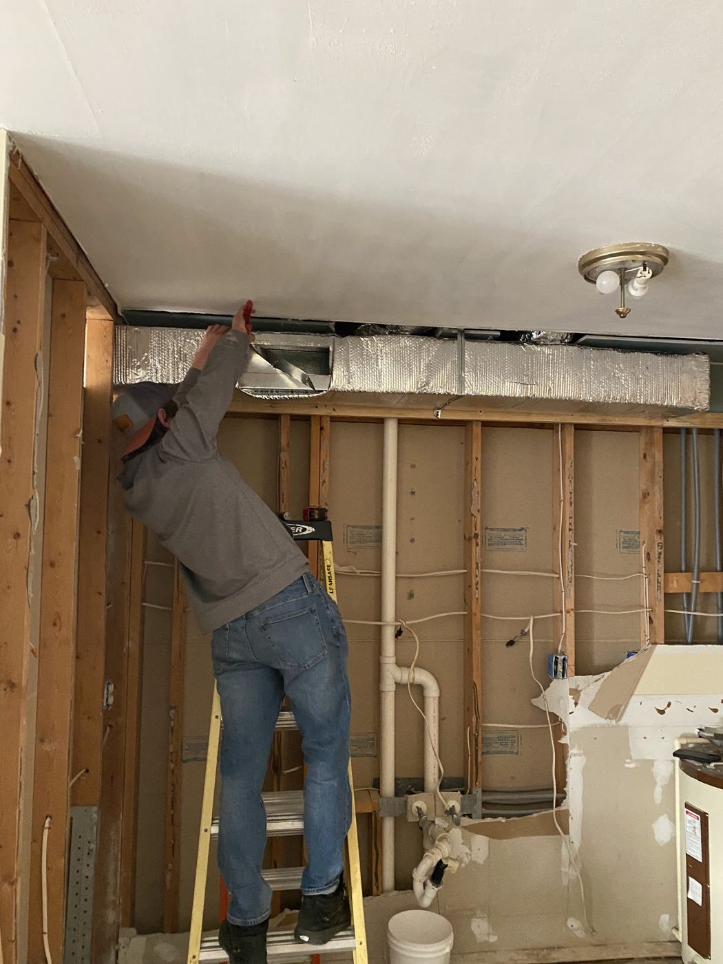 Technician installing ductwork in an open ceiling during a renovation